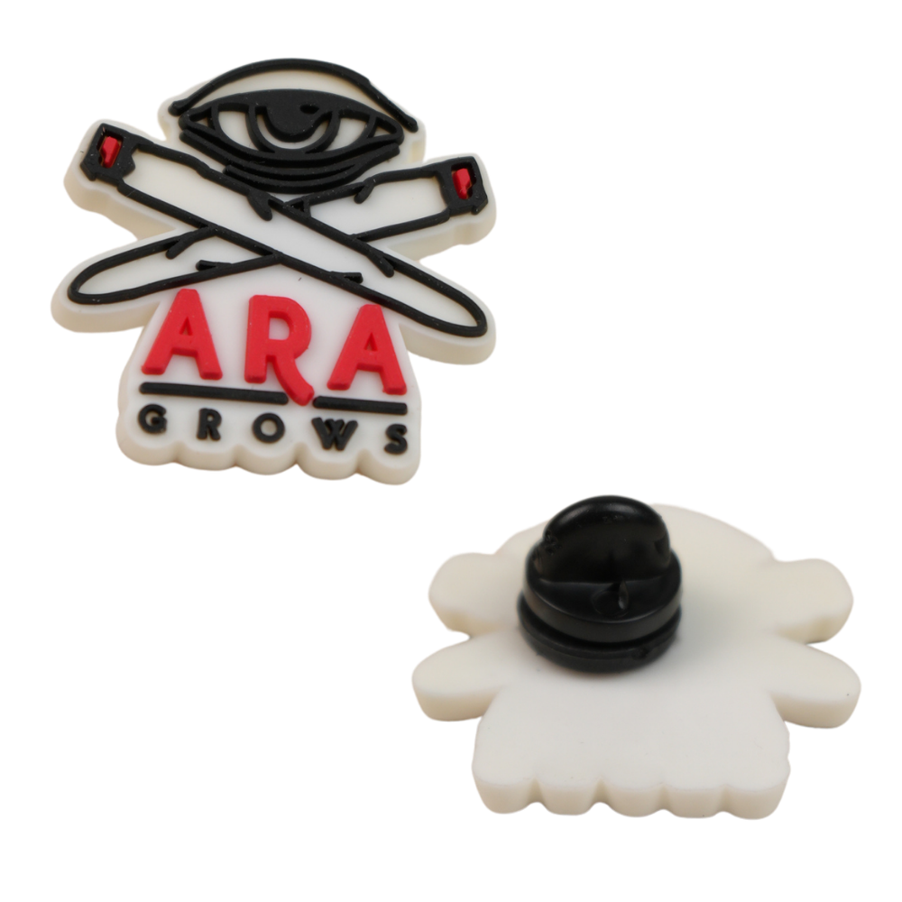 Pin de silicona ARA GROWS con diseño de ojo y blunts cruzados en colores blanco, negro y rojo.